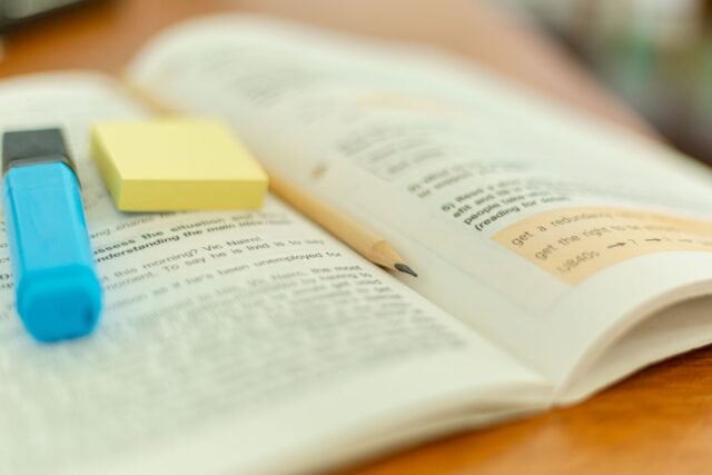 Manual deschis, cu un evidențiator și un caiet alături, pe un birou de studiu
